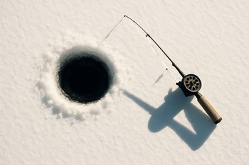 Dark round hole with the angler's shadow stretching over the ice
