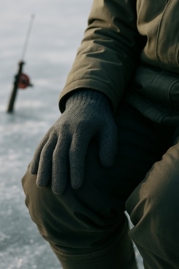 Angler's gloved hand resting calmly on a knee while sitting on the ice