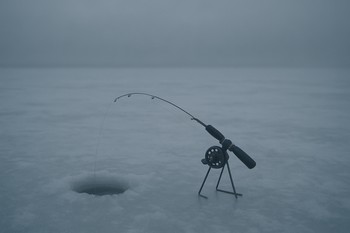 Ice fishing rod resting on a stand above an untouched hole