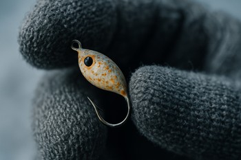 Hand holding a small ice lure between gloves